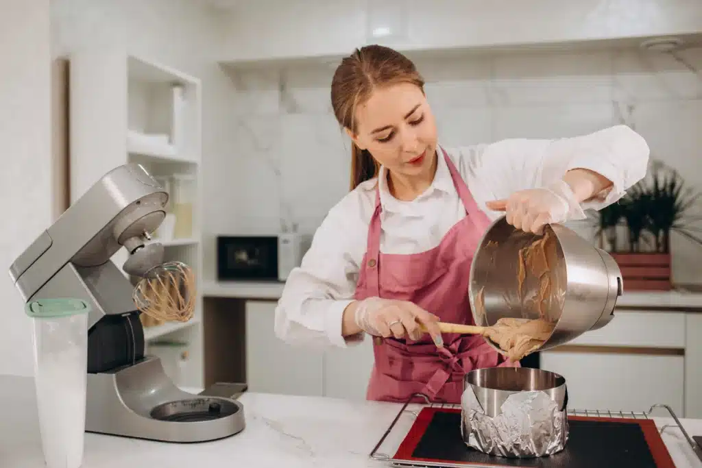 Amanda pouring thick cake batter into a round baking pan with foil lining