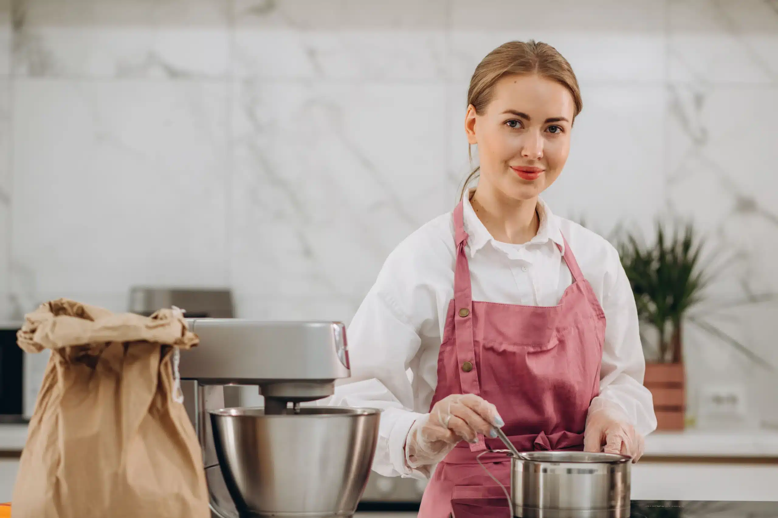 Amanda in a pink apron cooking with a stand mixer and saucepan in the kitchen
