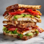 Healthy chicken club sandwich with bacon and avocado on toasted whole grain bread.